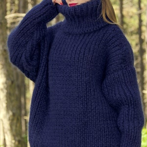 May include: A navy blue oversized turtleneck sweater with a fuzzy texture. The sweater is hand-knitted and has a loose, relaxed fit.
