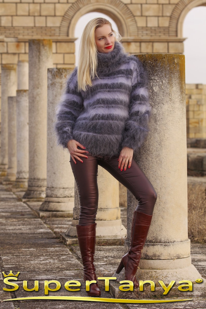 May include: A woman wearing a gray and white striped fuzzy turtleneck sweater, brown leather pants, and brown knee-high boots. The background features stone columns and arches.