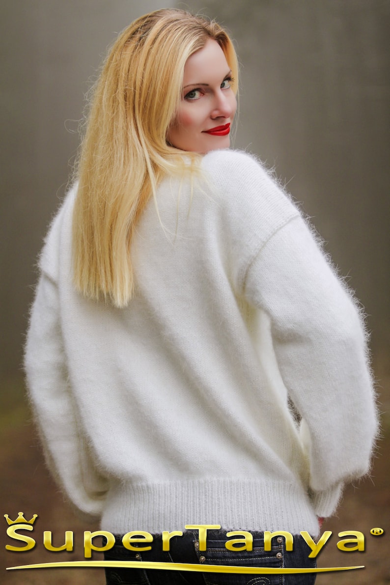 May include: A white fuzzy sweater with a ribbed hem. The sweater is made of a soft, fluffy material.