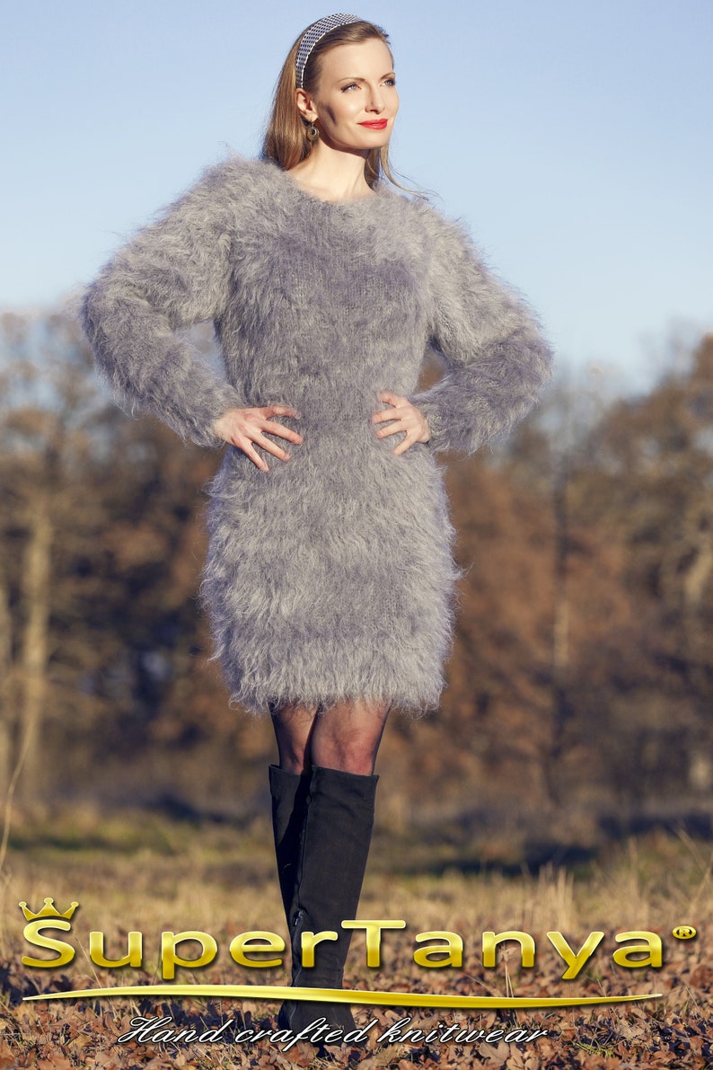 May include: A gray, fuzzy, long-sleeved dress. The dress is knee-length and has a round neckline. The model is wearing black boots. The image includes the text "SuperTanya" and "Hand crafted knitwear".