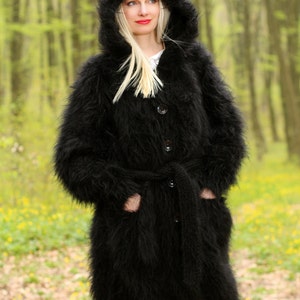 May include: A long black fuzzy knit cardigan with a hood, a belt, and buttons. The cardigan is worn by a person standing in a forest.