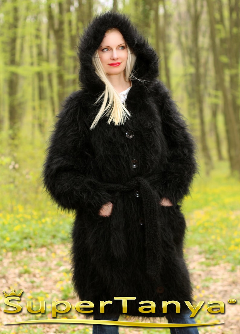 May include: A long black fuzzy knit cardigan with a hood, a belt, and buttons. The cardigan is worn by a person standing in a forest.