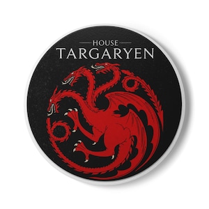 May include: A circular coaster with a black background featuring a red three-headed dragon emblem in the center. The text HOUSE TARGARYEN is printed in white capital letters above the dragon graphic. The coaster has a white border edge.