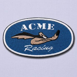 May include: An oval-shaped embroidered patch with a blue background and a white border. It features the white text ACME above a brown and black cartoon character graphic, with the white cursive text Racing positioned below the graphic.