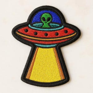 以下が含まれることがあります： 黒い縁取りが施された、空飛ぶ円盤の刺繍ワッペン。円盤には緑色の宇宙人が入った青いドーム、黒い円形のディテールがある赤い中央部、そして底から下に向かって伸びる黄色の光線がデザインされています。