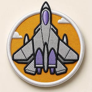 Peut inclure: Un écusson brodé circulaire représentant un avion de chasse gris avec des accents violets sur un fond orange vif. Le motif comprend deux petits nuages blancs et est encadré par une bordure blanche épaisse, avec des coutures détaillées.