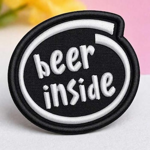 Könnte beinhalten: Ein kreisförmiger gestickter Aufnäher mit schwarzem Hintergrund und einem dicken weißen Rand. Der Text "beer inside" ist in weißen, kleingeschriebenen, serifenlosen Buchstaben in der Mitte des Aufnähers eingestickt und folgt der Kreisform.