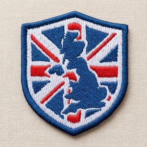 Puede incluir: Un parche bordado en forma de escudo que presenta una silueta azul oscuro del mapa del Reino Unido sobre un patrón de bandera Union Jack en rojo, blanco y azul. El parche tiene un borde grueso cosido en azul oscuro y una textura de tela.