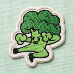 May include: An embroidered patch featuring a cartoon broccoli character with a dark green top and light green stem. The character has a determined facial expression, black outlines, and is posed in a dynamic kick. The patch has a white border.