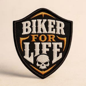 Op de afbeelding: Een schildvormige geborduurde patch met een zwarte achtergrond en een dikke zwarte rand. De tekst BIKER FOR LIFE is geborduurd met wit en goudkleurig garen. Een witte schedelafbeelding bevindt zich onderaan in het midden van het ontwerp.