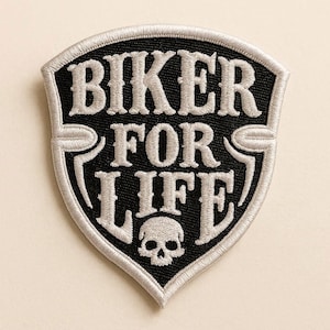 Puede incluir: Un parche bordado en forma de escudo con fondo negro y borde plateado. El texto BIKER FOR LIFE está bordado con hilo plateado en una fuente serif negrita. Debajo del texto, un pequeño icono de calavera plateada detallada está centrado en la parte inferior.