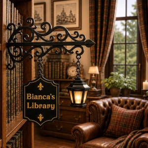Può includere: Un'insegna da parete in metallo nero con volute ornamentali, dotata di una targa rettangolare sospesa con il testo "Bianca's Library" in lettere dorate e una piccola lanterna laterale che emana una luce calda.