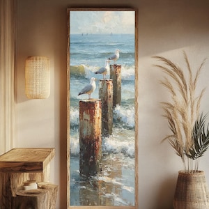 May include: A vertical rectangular framed oil painting depicting three white and grey seagulls perched on weathered, rust-colored wooden pilings rising from a blue ocean with white-capped waves under a soft, light-filled sky with distant sailboats.