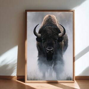 May include: A framed wall art print featuring a front-facing American bison with dark brown fur, curved horns, and a thick mane. The animal stands in a misty, atmospheric landscape with tall grass visible at the bottom of the composition.