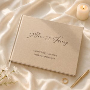 Puede incluir: Un libro de visitas rectangular cubierto de tela beige con el texto impreso Alice & Harry, Kirkby Fleetham Hall y 29th November 2025 en color marrón oscuro. La cubierta tiene un diseño rígido y limpio con un acabado de textura suave.