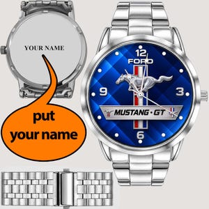 May include: A silver-toned stainless steel wristwatch featuring a blue dial with a Ford Mustang GT logo, a running horse emblem, and white numerals. The watch includes a metal link band and a customisable case back with the text YOUR NAME.
