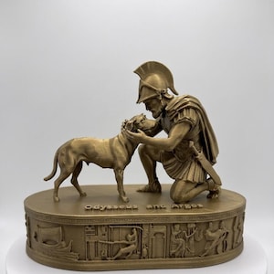 May include: A gold-colored statue depicting a kneeling warrior in a helmet and armor petting a dog. The base features the text "Odysseus and Argos" and a relief carving of ancient scenes including a ship and figures in various poses.
