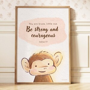May include: A framed wall art print featuring a watercolour illustration of a brown monkey. The text reads: You are brave, little one. Be strong and courageous. Joshua 1:9. The background includes a soft peach-coloured watercolour wash.