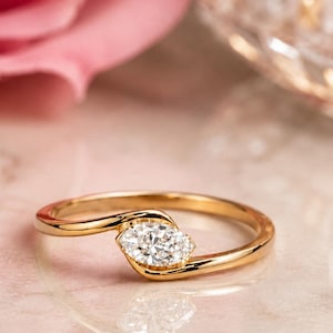 Peut inclure: Une bague en or avec une pierre précieuse transparente unique taillée en marquise, montée sur un anneau de style bypass. L'anneau en or jaune poli s'incurve autour de la pierre centrale, créant un design fluide qui met en valeur la forme.