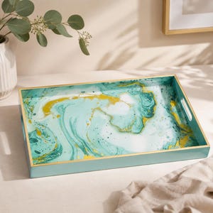 May include: A rectangular serving tray featuring a marbled pattern in shades of teal, white, and gold. The tray has a smooth, glossy interior surface with a solid light blue exterior frame and integrated cutout handles on the shorter sides.