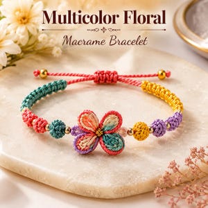May include: A macrame bracelet featuring a central flower motif with petals in shades of pink, orange, and teal. The band consists of knotted cord in teal, red, yellow, and purple, accented with small gold-toned beads and a sliding knot closure.