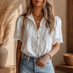 May include: A white short-sleeved button-down shirt featuring intricate lace trim along the front placket and sleeve cuffs. The shirt is paired with light blue denim jeans. A gold-toned necklace with a floral pendant is worn around the neck.