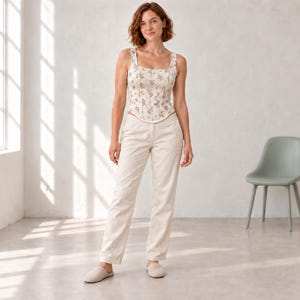 May include: A sleeveless corset-style top featuring a cream base with a delicate brown floral pattern, paired with straight-leg cream trousers and light-colored slip-on shoes. The top has a square neckline and a structured bodice.