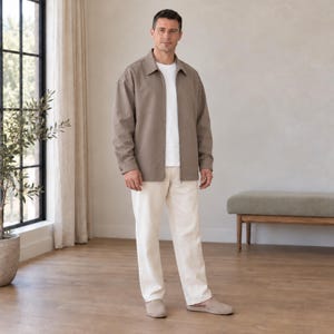 Könnte beinhalten: Eine taupefarbene Reißverschlussjacke mit Kragen über einem schlichten weißen T-Shirt, kombiniert mit einer cremeweißen Hose und hellbeigen Slipper-Schuhen. Die Jacke hat lange Ärmel und einen geraden Saum für ein neutrales Outfit.