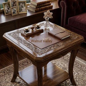Op de afbeelding: Een vierkante houten bijzettafel met ingewikkelde bloemmotieven langs de randen, voorzien van een onderste plank, een bruine lederen bureaulegger met de tekst Walnut Valley, een kleine glazen vaas met een bloem, een houten inktpotset en een bruin notitieboek.