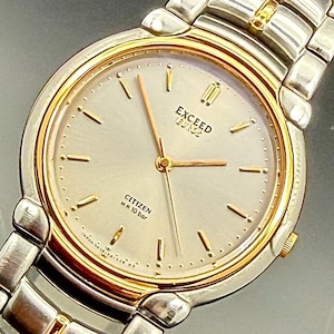 May include: A Citizen Exceed wristwatch with a round silver dial, gold-tone hour markers, and gold-tone hands. The watch features a two-tone silver and gold metal link bracelet, a gold-tone bezel, and text on the dial reading EXCEED and W.R 10 bar.