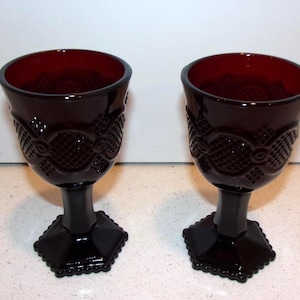 May include: Two ruby red goblets with intricate embossed patterns on the bowl and a black stem and base. The goblets have a deep red interior and are set against a white background. The stem is approximately 4 inches tall.