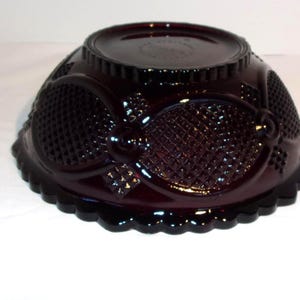 May include: A dark red, decorative glass bowl with a scalloped edge. The bowl features an intricate pattern of oval and diamond shapes. The bowl is likely vintage and is made of pressed glass.