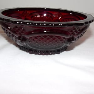 May include: A deep red glass bowl featuring a pressed diamond pattern on the exterior, a scalloped rim with a beaded edge, and circular accents along the sides. The bowl has a translucent quality and a smooth, reflective surface finish.