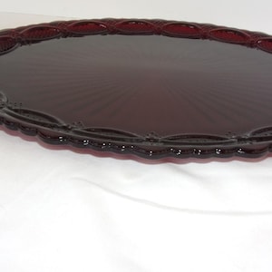May include: A ruby red oval serving platter with a decorative, scalloped edge. The center of the platter features a sunburst design. The platter is made of glass and is likely vintage. A beautiful piece for serving food.