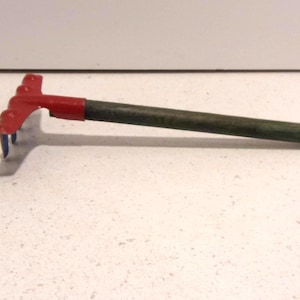 May include: A small garden hand rake with a red head and handle attachment, and a dark green wooden handle. The rake's tines are blue. The tool is designed for gardening and landscaping tasks.