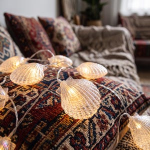 May include: A string of decorative lights featuring translucent, ribbed seashell-shaped covers. Each shell houses a warm, glowing bulb connected by a thin, clear wire. The shells are arranged in a series, emitting a soft, golden light.