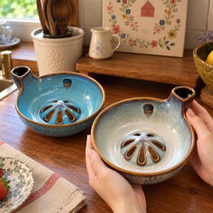 May include: Two ceramic berry bowls with a reactive glaze finish. One bowl features a vibrant blue hue, while the other transitions from a light cream centre to a blue rim. Both bowls include a central drainage grate and a side pouring spout.