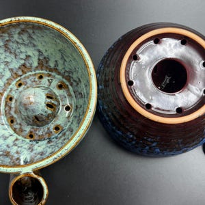 May include: A ceramic coffee dripper shown from two angles. The left side displays the interior with a light blue and brown mottled glaze and a central drainage cone. The right side shows the dark brown and blue exterior base with drainage holes.