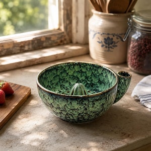 May include: A ceramic citrus juicer bowl featuring a vibrant green and black mottled glaze. The bowl has a central raised reamer for extracting juice and a small integrated handle on the side, showcasing a textured, glossy finish throughout.