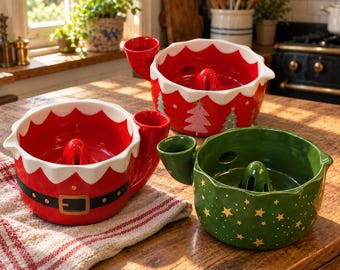 May include: Three ceramic citrus juicers with handles. One is red with a black belt and gold buckle, one is red with white trim and green trees, and one is green with gold stars. Each features a central reamer and a pouring spout.