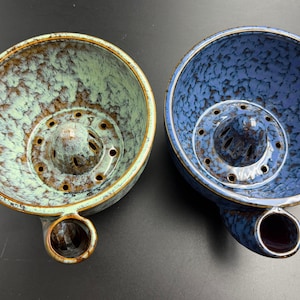 May include: Two ceramic citrus juicers with a speckled glaze finish. One juicer is light green with brown accents, and the other is blue with dark blue speckles. Both feature a central reamer with drainage holes and a side spout.