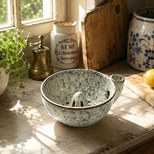 May include: A ceramic citrus juicer bowl featuring a white and black crackle glaze finish. The bowl has a central reamer cone for extracting juice and a small side handle. The exterior and interior surfaces display a textured, mottled pattern.
