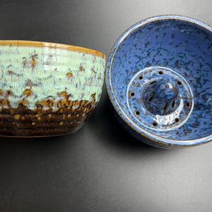 May include: Two ceramic bowls with a speckled glaze. The bowl on the left features a light mint green upper section transitioning into a dark brown base. The bowl on the right is blue with a central raised dome containing small drainage holes.