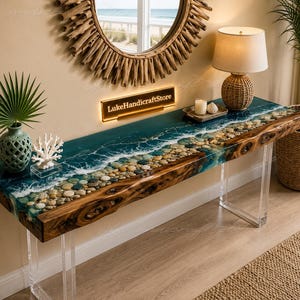 Könnte beinhalten: Ein rechteckiger Konsolentisch mit einer Naturholzkante und einer blauen Harzeinlage, die Meereswellen und einen Kieselstrand nachahmt. Der Tisch hat klare Acrylbeine und ein an der Wand montiertes Schild mit der Aufschrift LukeHandicraftStore.