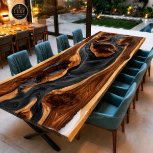 Op de afbeelding: Een grote rechthoekige eettafel met een houten blad met natuurlijke randen en een centraal rivierontwerp van donkere, wervelende hars. De tafel rust op een zwart metalen X-vormig onderstel en is omringd door diverse blauwgroene gestoffeerde stoelen.