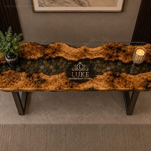 Könnte beinhalten: Ein rechteckiger Konsolentisch mit einer Naturholzkante und einer flussartigen Einlage aus glatten, dunklen Kieselsteinen in klarem Harz. Der Tisch hat schwarze Metallbeine und trägt den Schriftzug LUKE HANDICRAFT STORE.