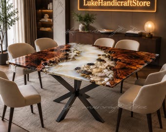 May include: A square dining table featuring a polished resin surface with a central river design filled with smooth, multi-coloured stones and dark wood grain patterns, supported by a black metal X-shaped base, surrounded by eight beige chairs.