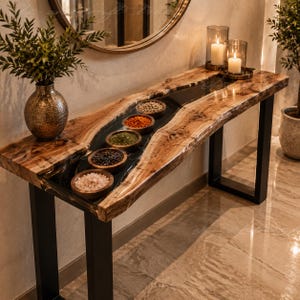 Pode incluir: Uma mesa consola de madeira com borda natural e uma incrustação central de resina preta, contendo cinco pequenas tigelas de madeira com várias especiarias. A mesa tem pernas de metal preto, dois castiçais de vidro e um vaso texturizado.