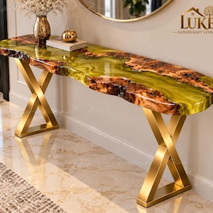 Può includere: Un tavolo console con bordo in legno naturale e un inserto in resina verde lime traslucida. Il tavolo è sostenuto da due gambe in metallo dorato a forma di X. La superficie presenta una finitura lucida e le venature del legno naturale.
