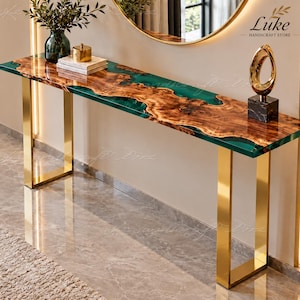 Puede incluir: Una mesa consola con un tablero de madera de borde natural y veteado visible, incrustado en resina verde esmeralda translúcida. La mesa se apoya sobre dos patas de metal dorado pulido en forma de U y muestra el texto Luke Handicraft Store.